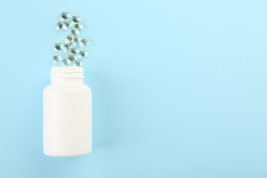 Bottle and vitamin capsules on light blue background, top view. Space for text