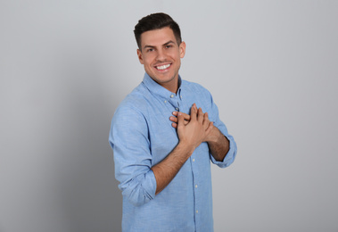 Photo of Handsome grateful man with hands on chest against light grey background