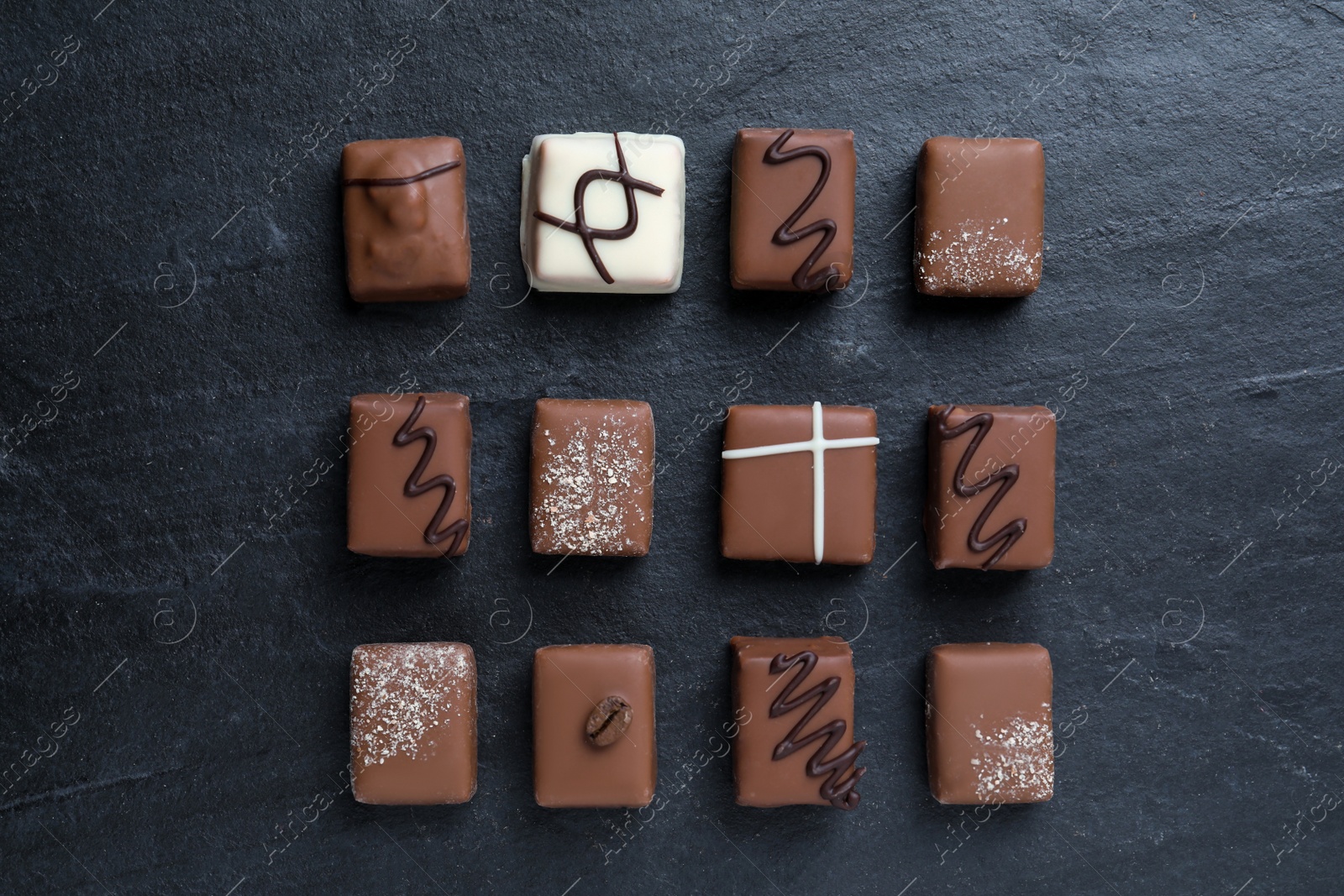 Photo of Different delicious chocolate candies on black table, flat lay