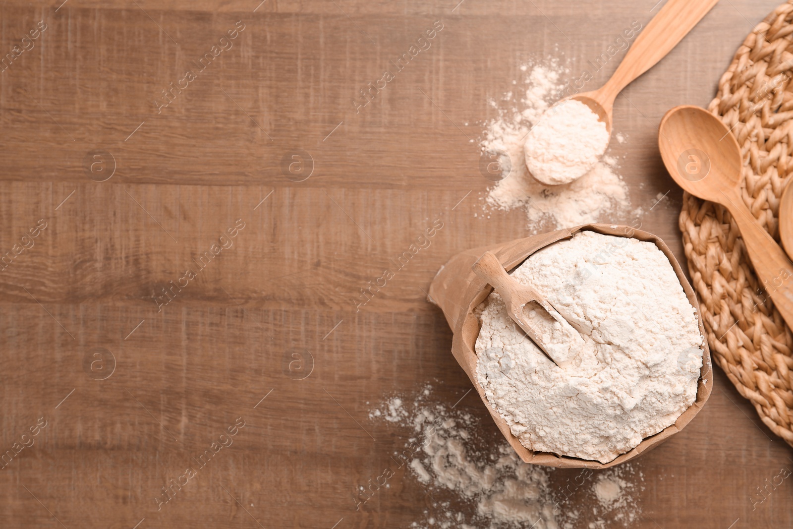 Photo of Paper bag and spoon with flour on wooden background, top view