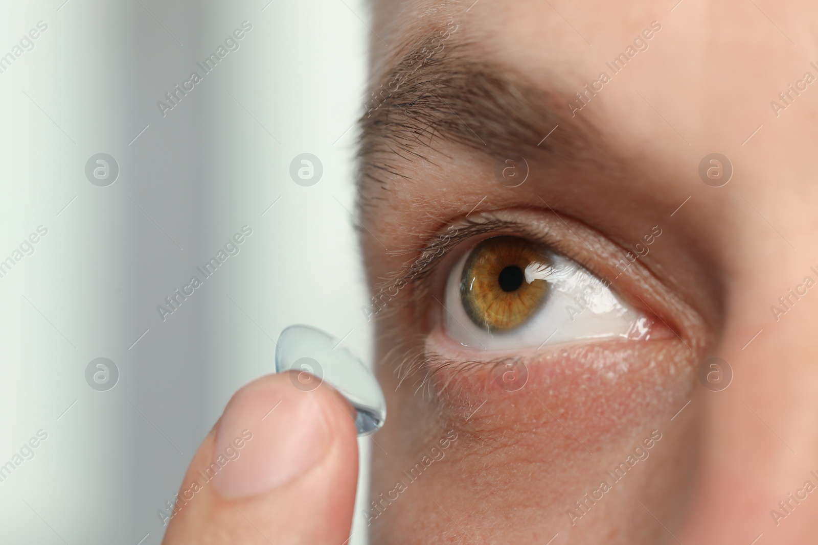 Photo of Man putting contact lens in his eye on blurred background, closeup