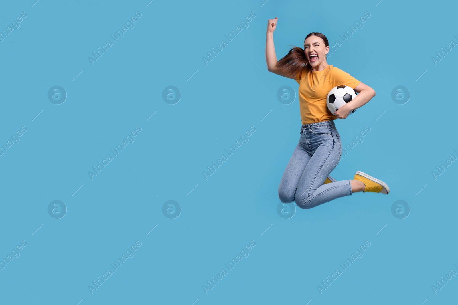 Photo of Happy soccer fan with ball jumping on light blue background. Space for text