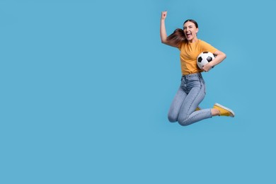 Photo of Happy soccer fan with ball jumping on light blue background. Space for text