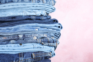 Stack of different jeans on pink background, closeup