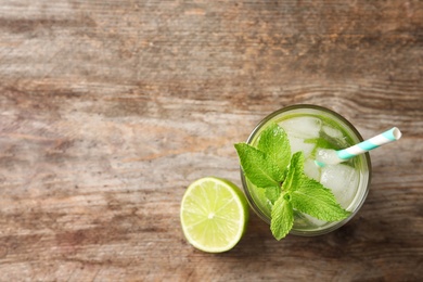 Refreshing beverage with mint and lime in glass on wooden background, top view