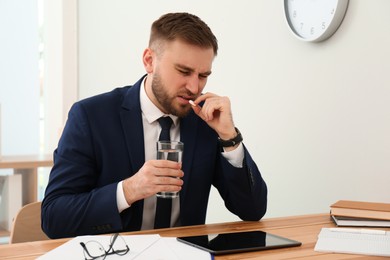 Photo of Man taking pill against migraine in office