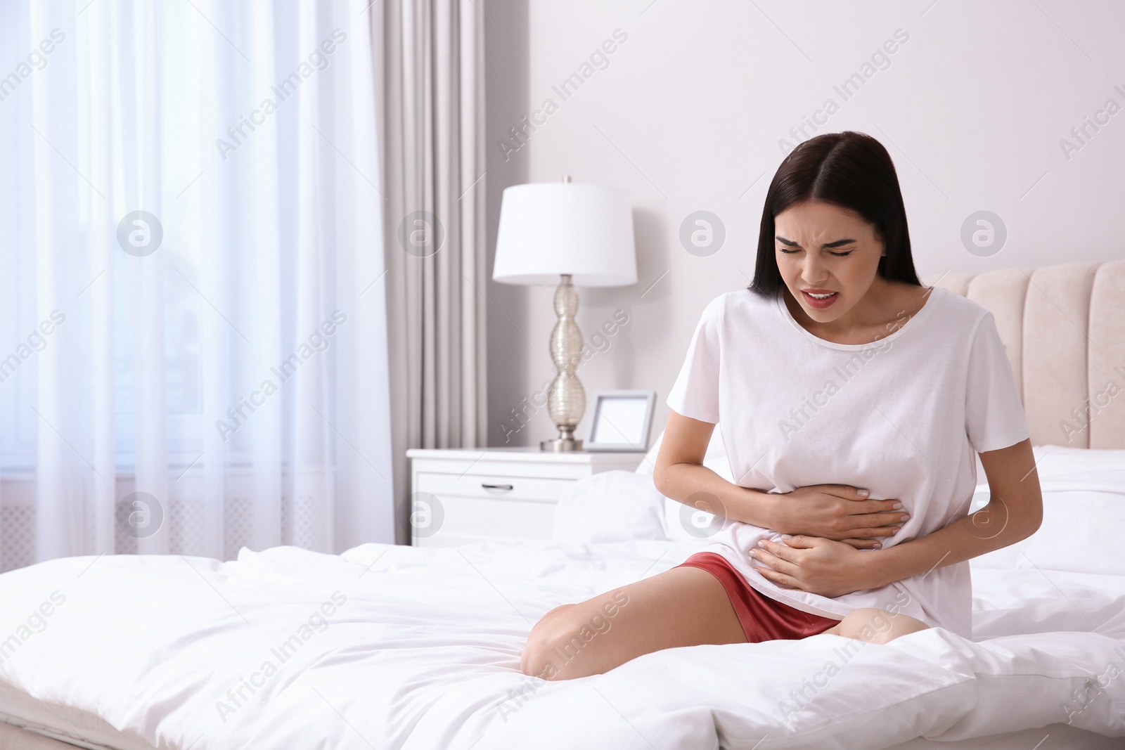 Photo of Young woman suffering from stomach ache in bedroom