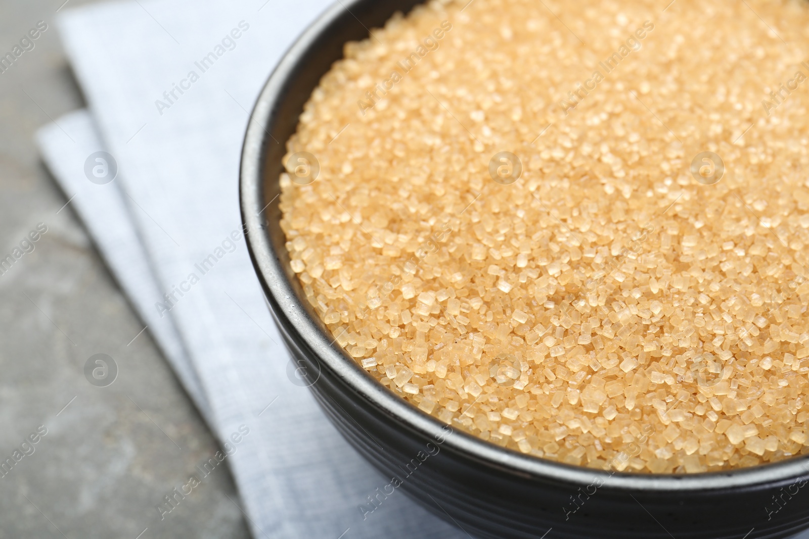 Photo of Brown sugar in bowl on grey table, closeup. Space for text