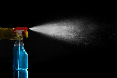 Photo of Woman spraying liquid from bottle on black background, closeup