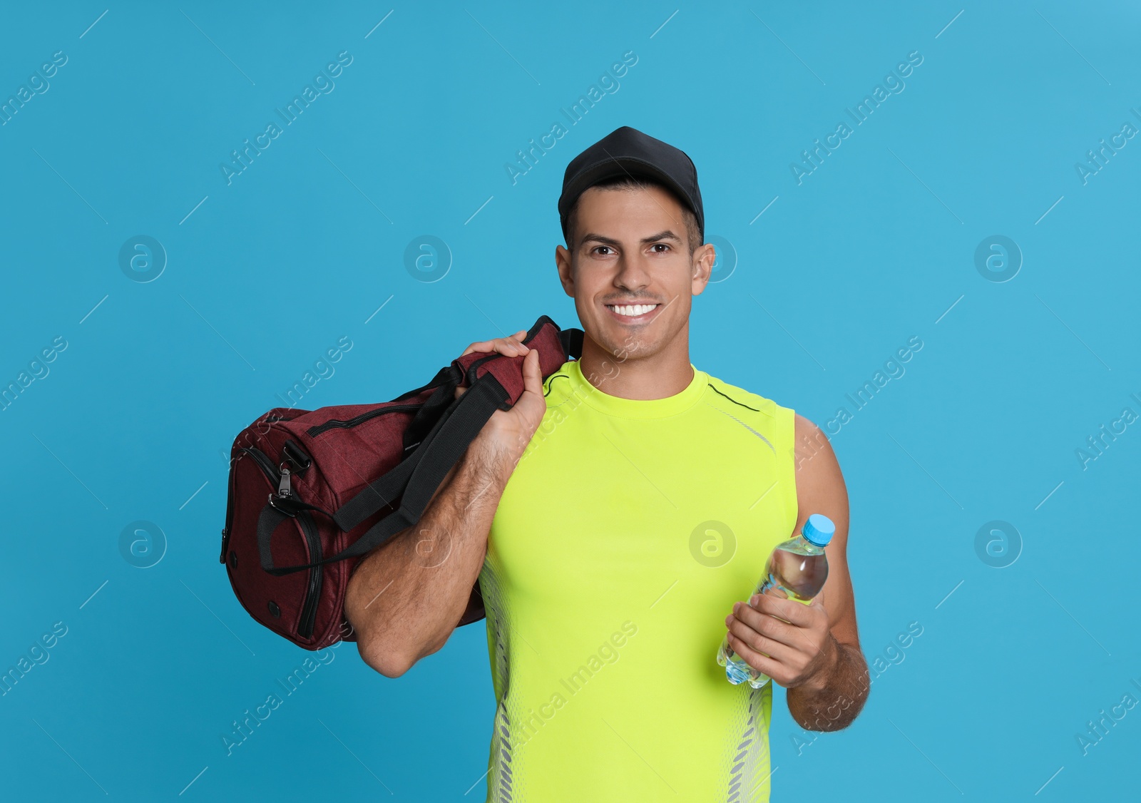 Photo of Handsome man with sports bag and bottle of water on light blue background