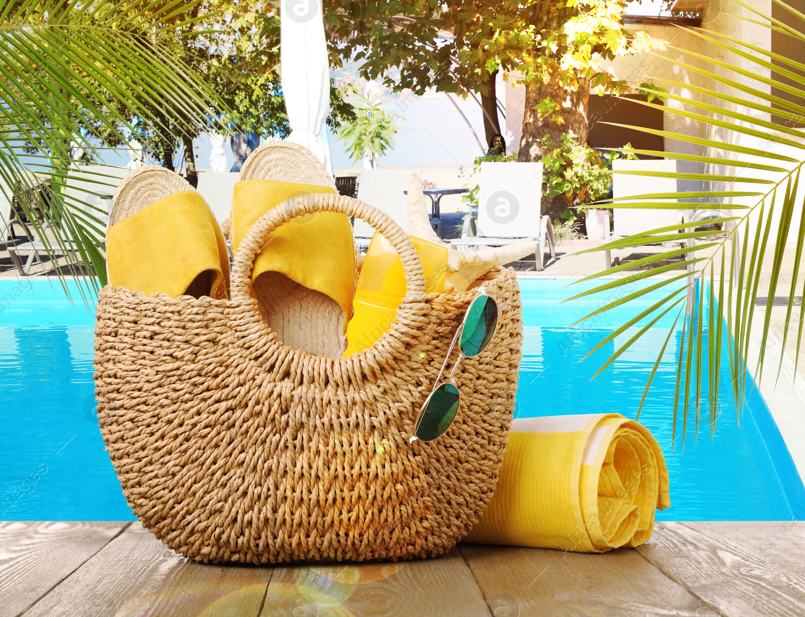 Image of Stylish bag with beach accessories on wooden surface near outdoor swimming pool