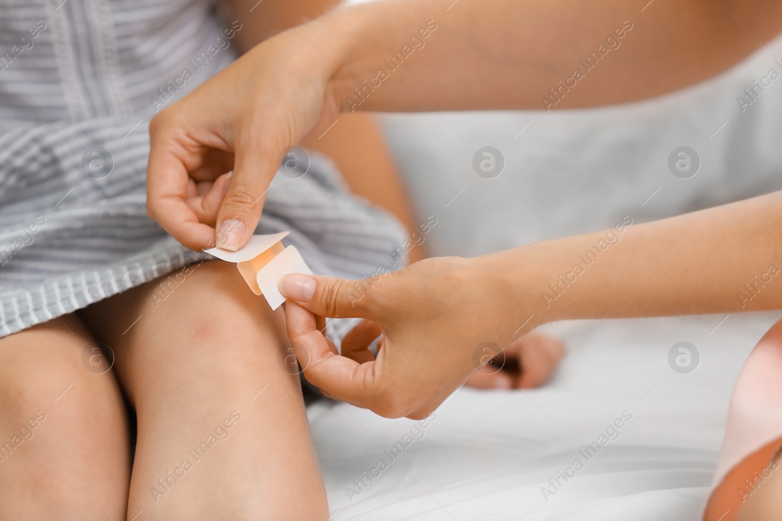 Photo of Woman applying plaster on girl's knee, closeup view