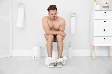 Photo of Young naked man suffering from diarrhea on toilet bowl at home