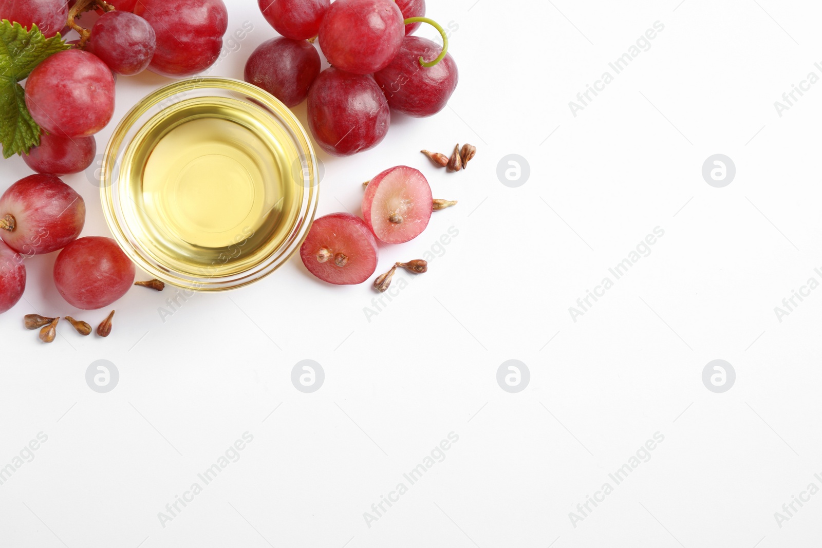 Photo of Organic red grapes, seeds and bowl of natural essential oil on white background, flat lay. Space for text