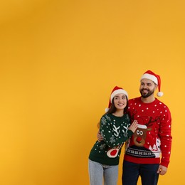 Photo of Happy young couple in Christmas sweaters and Santa hats on orange background. Space for text