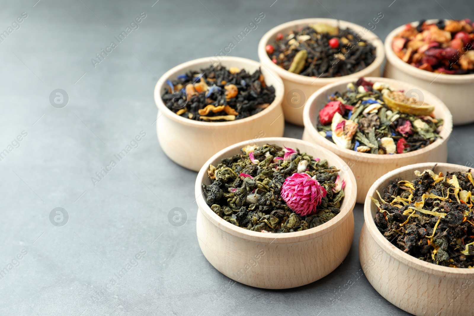 Photo of Different kinds of dry herbal tea in wooden bowls on light grey table. Space for text