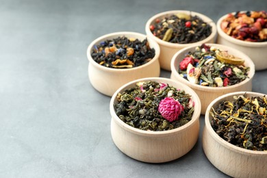 Photo of Different kinds of dry herbal tea in wooden bowls on light grey table. Space for text