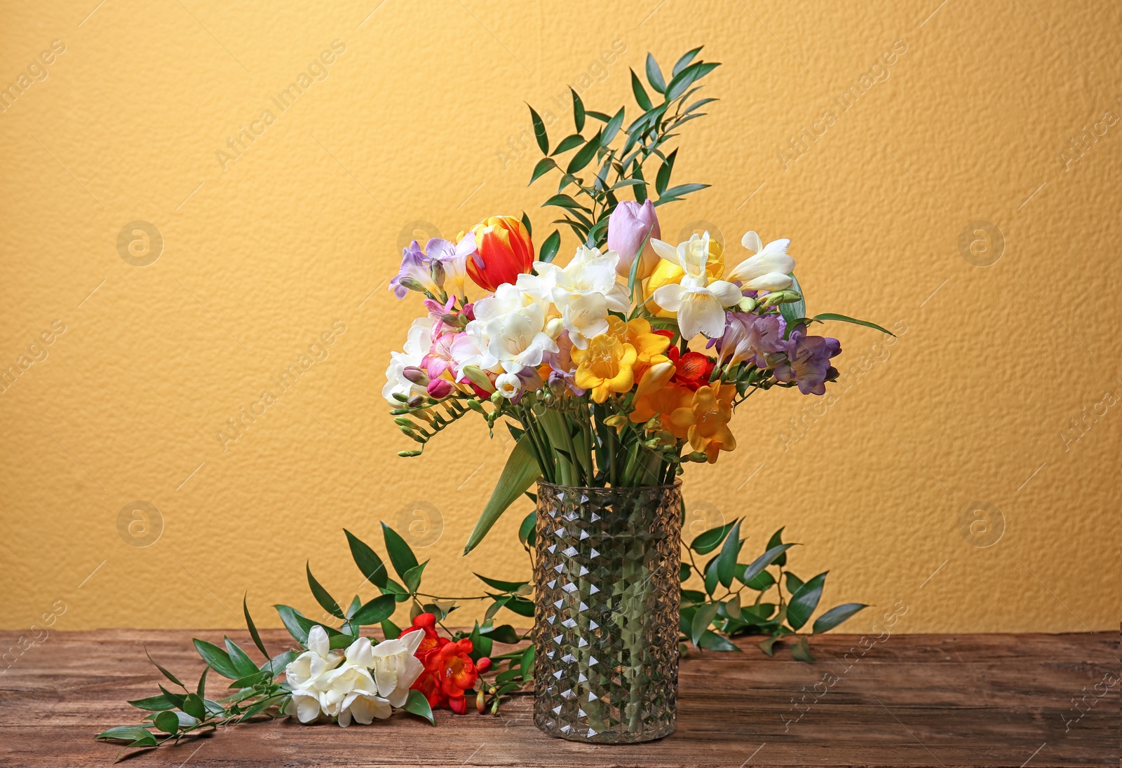 Photo of Glass vase with beautiful freesia flowers on table against color background