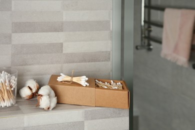 Photo of Cotton swabs and flowers on tiled surface in bathroom