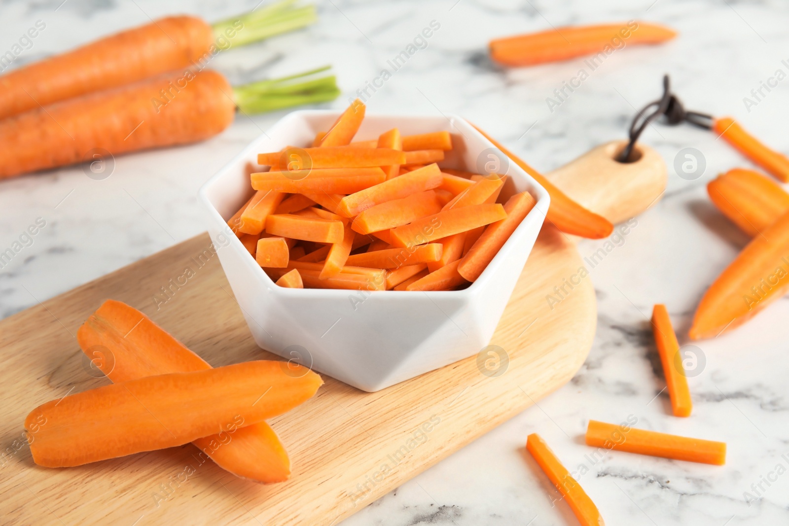 Photo of Bowl with cut ripe carrot on wooden board