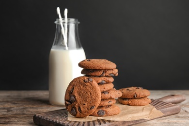Photo of Stack of tasty chocolate chip cookies and bottle of milk on wooden table
