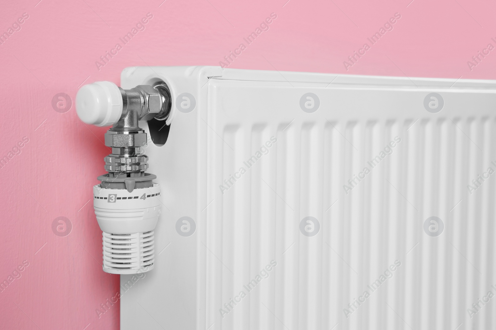 Photo of Heating radiator with thermostat near color wall