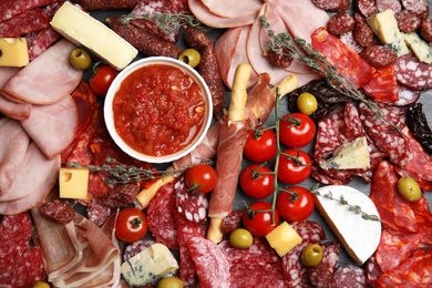 Tasty ham with other delicacies on black table, flat lay