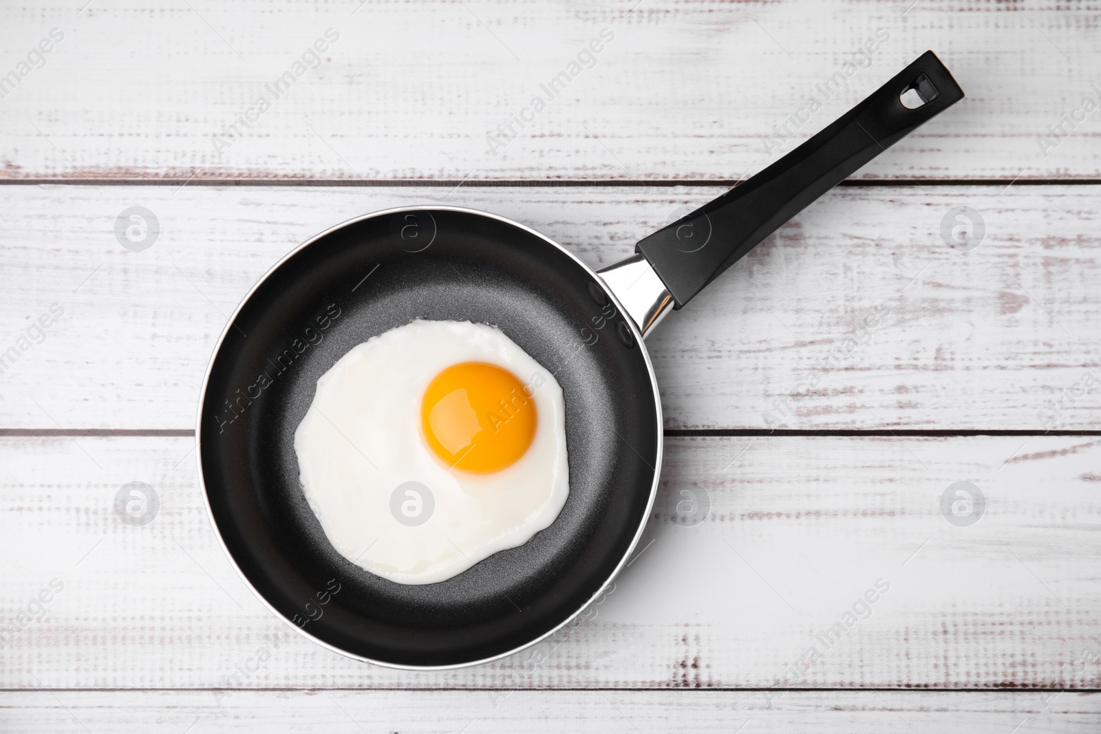 Photo of Tasty fried egg in pan on white wooden table, top view