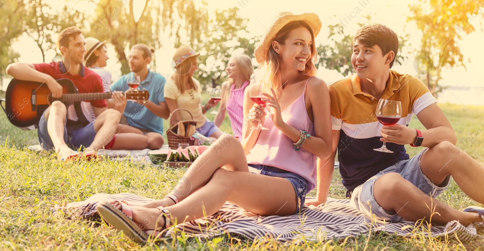 Image of Happy friends having picnic in park on sunny day