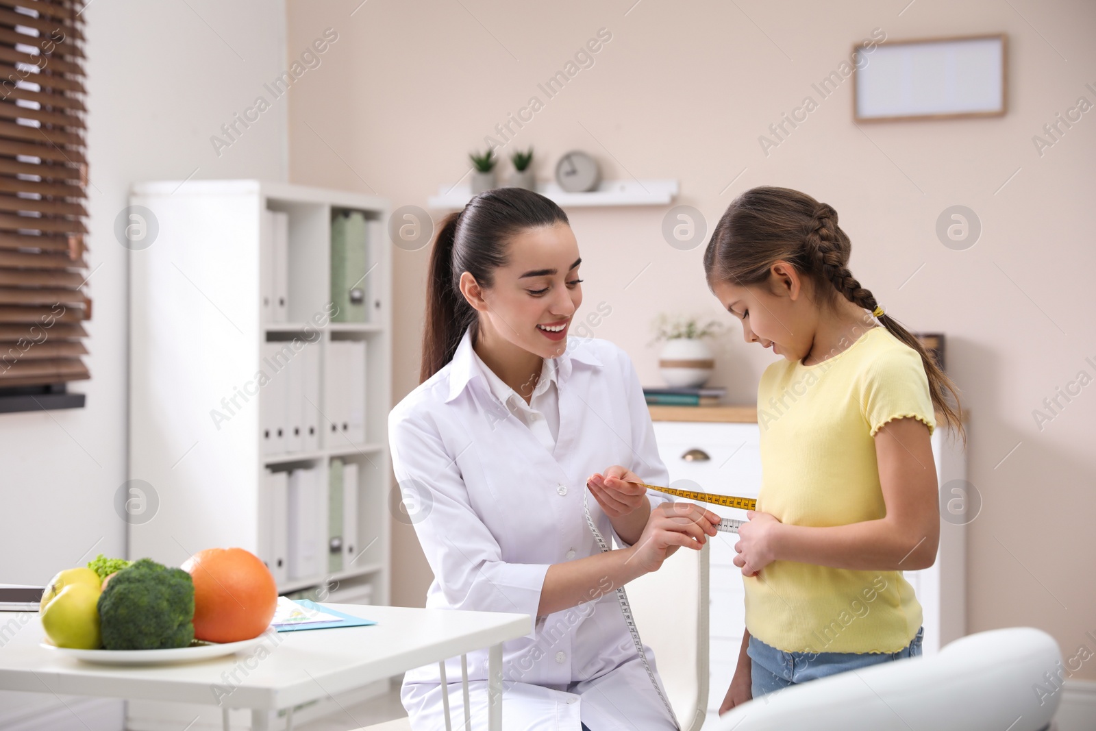Photo of Professional nutritionist measuring waist of little girl in office