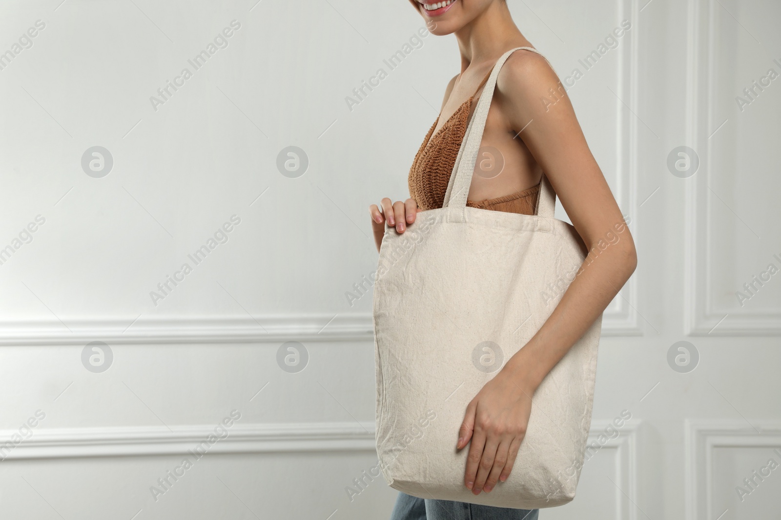 Photo of Happy young woman with blank eco friendly bag near white wall, closeup. Space for text