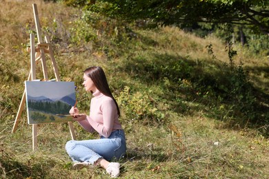 Photo of Young woman drawing on easel with brush outdoors, space for text