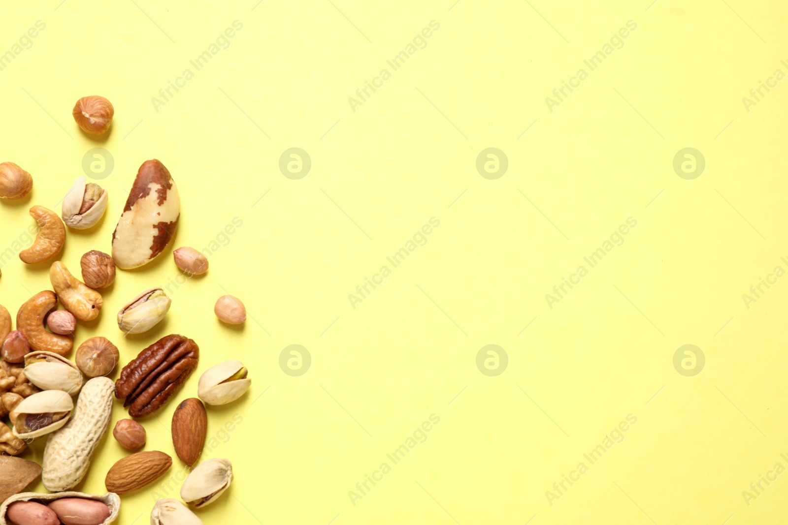 Photo of Different delicious nuts on yellow background, flat lay. Space for text