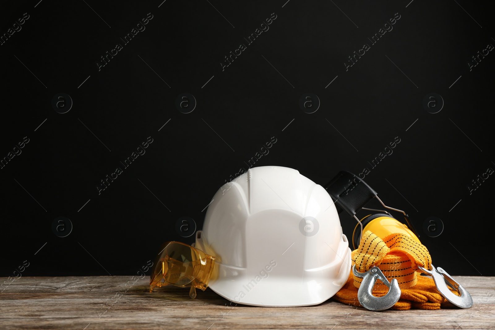 Photo of Different safety equipment on wooden table against black background. Space for text