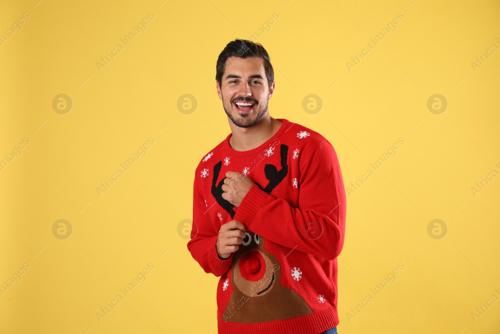 Photo of Portrait of happy young man in Christmas sweater on yellow background