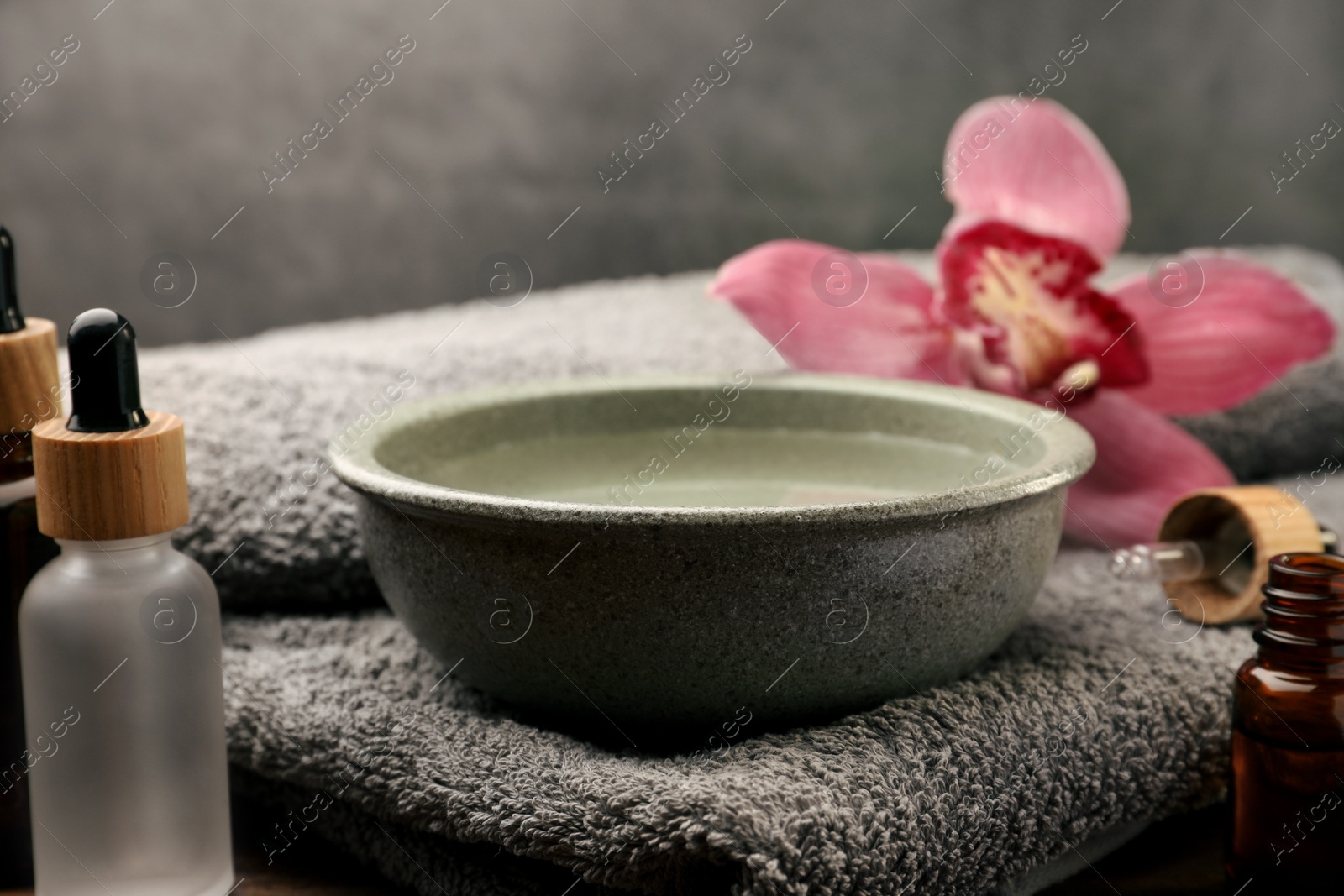 Photo of Bowl of essential oil and beautiful flower on wooden table. Aromatherapy treatment