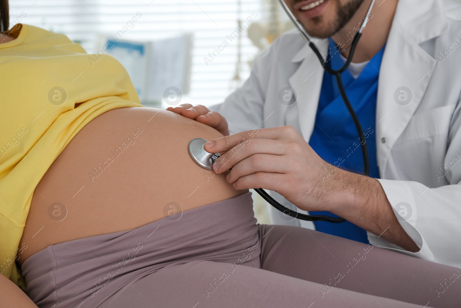 Photo of Doctor examining pregnant woman with stethoscope in clinic, closeup