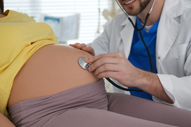 Doctor examining pregnant woman with stethoscope in clinic, closeup