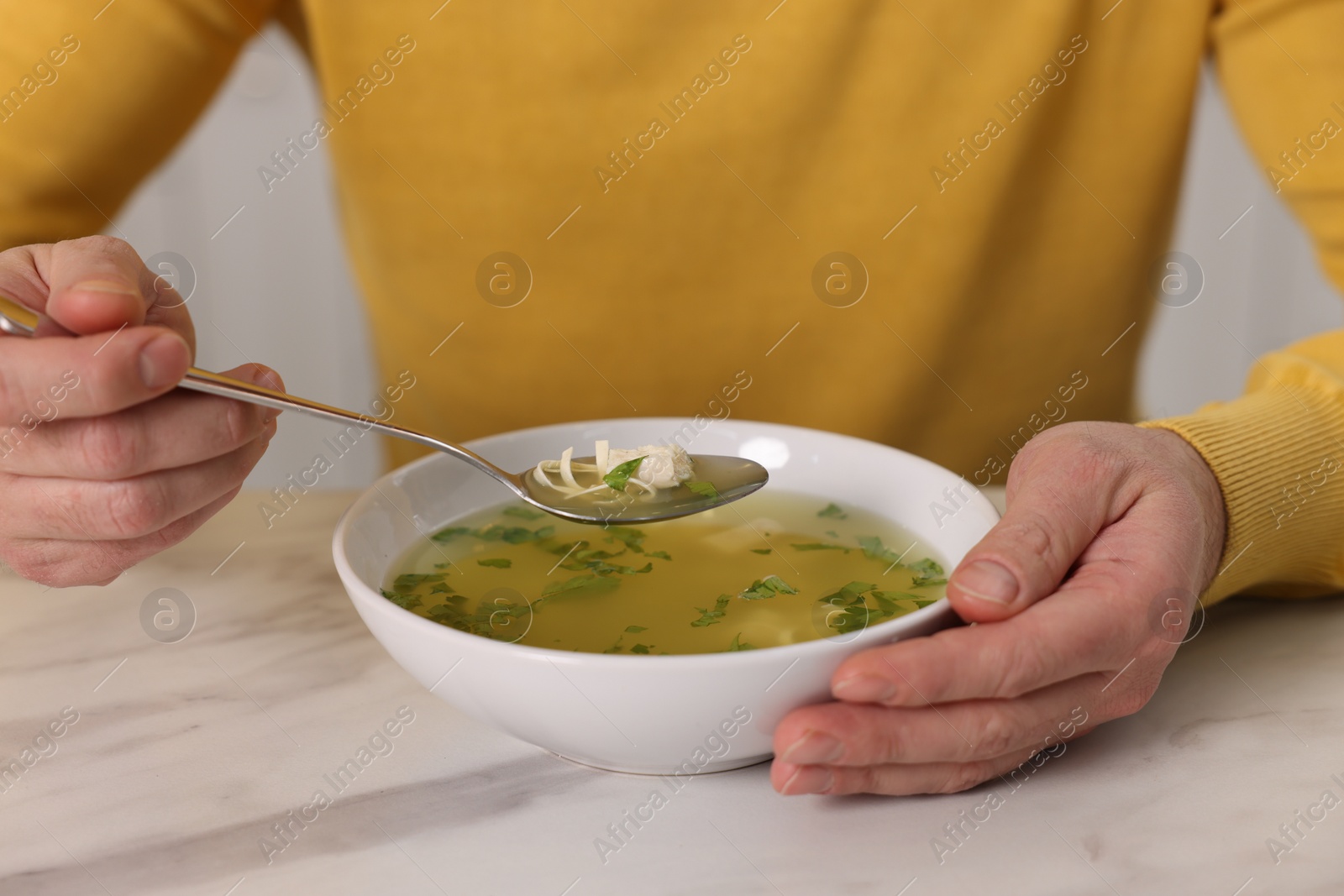 Photo of Man eating delicious chicken soup at light marble table, closeup