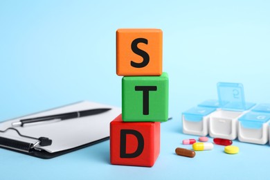 Photo of Abbreviation STD made with cubes on light blue background