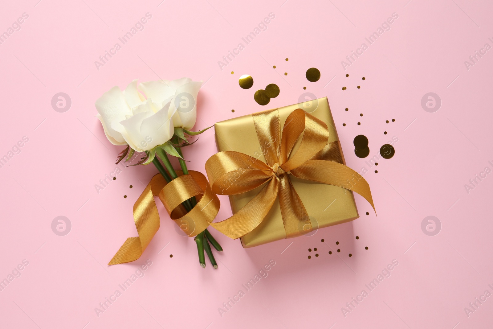 Photo of Beautiful golden gift box, flowers and confetti on pink background, flat lay