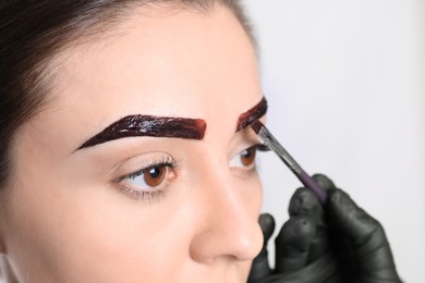 Photo of Beautician applying tint during eyebrows correction procedure on light background, closeup