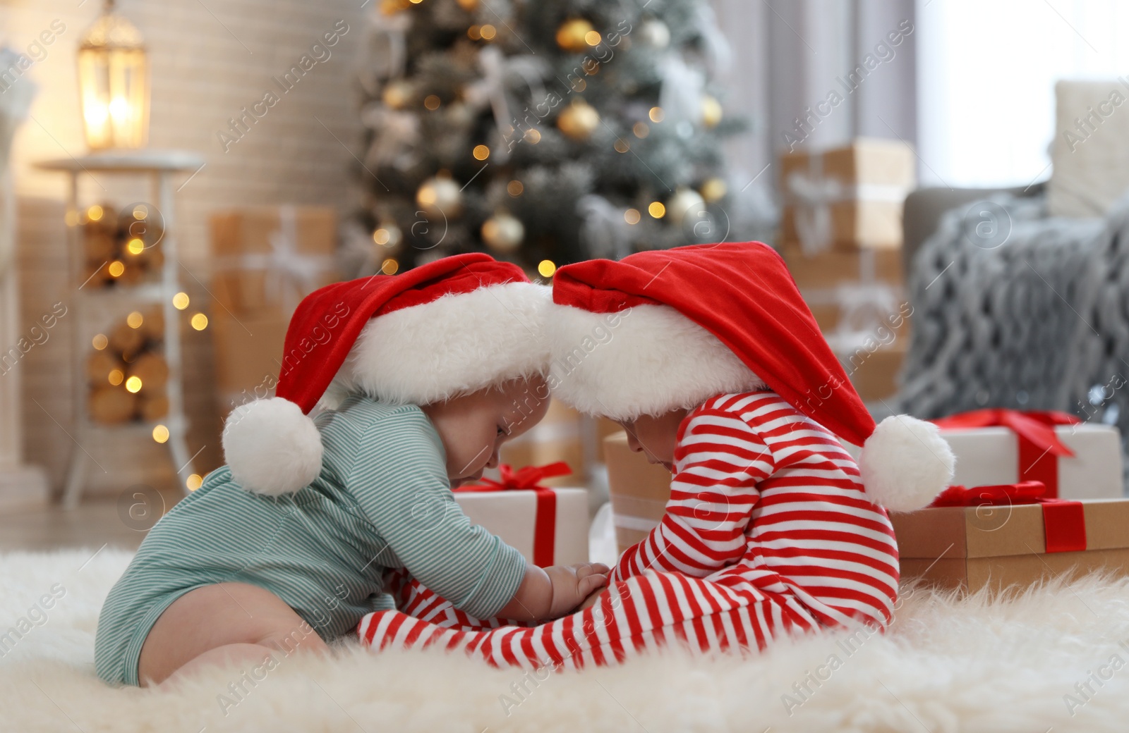 Image of Cute children in Santa hats on floor in room with Christmas tree