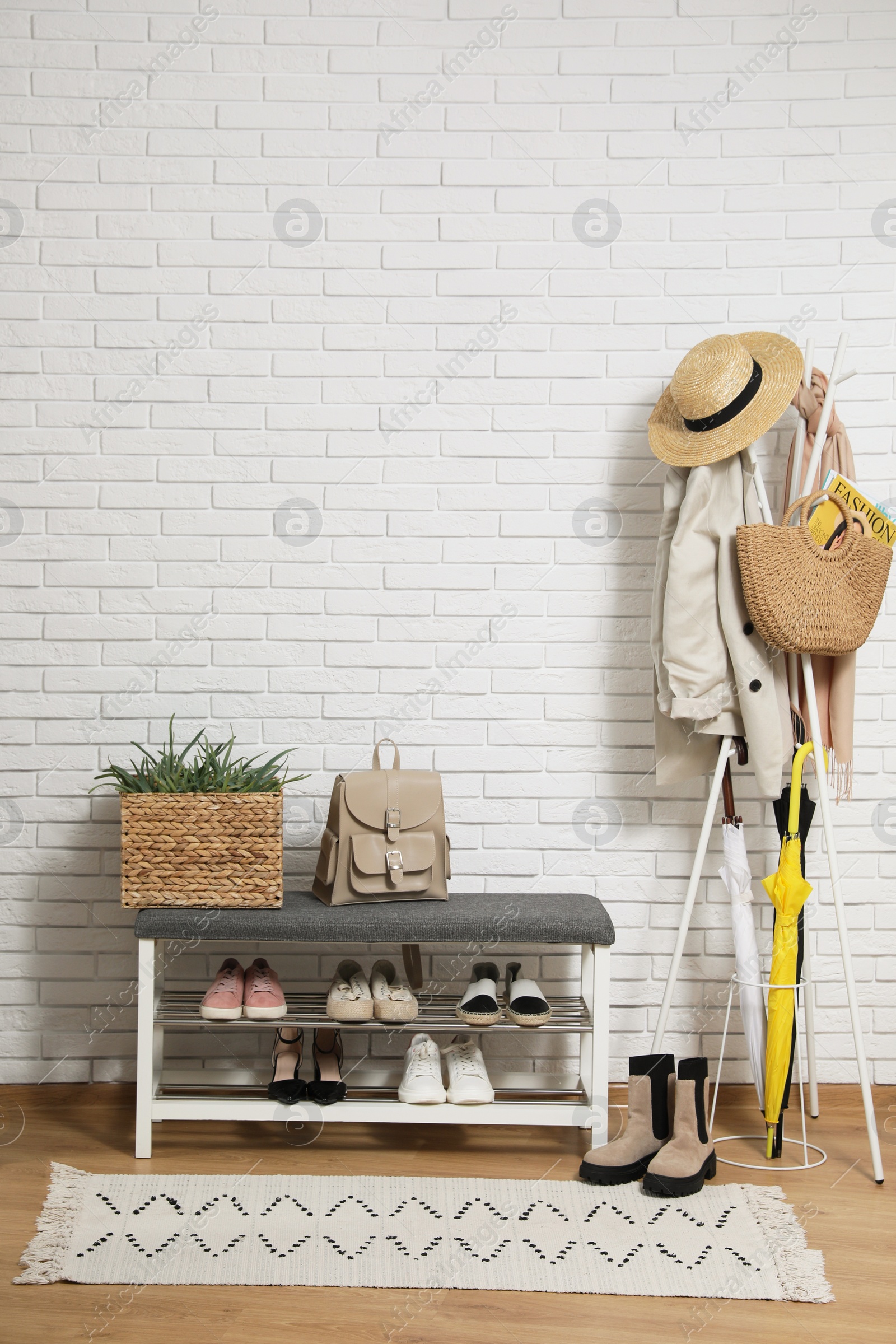 Photo of Stylish hallway interior with coat rack and shoe storage bench near white brick wall