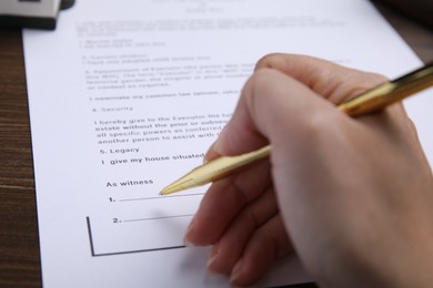 Photo of Woman signing last will and testament at table, closeup