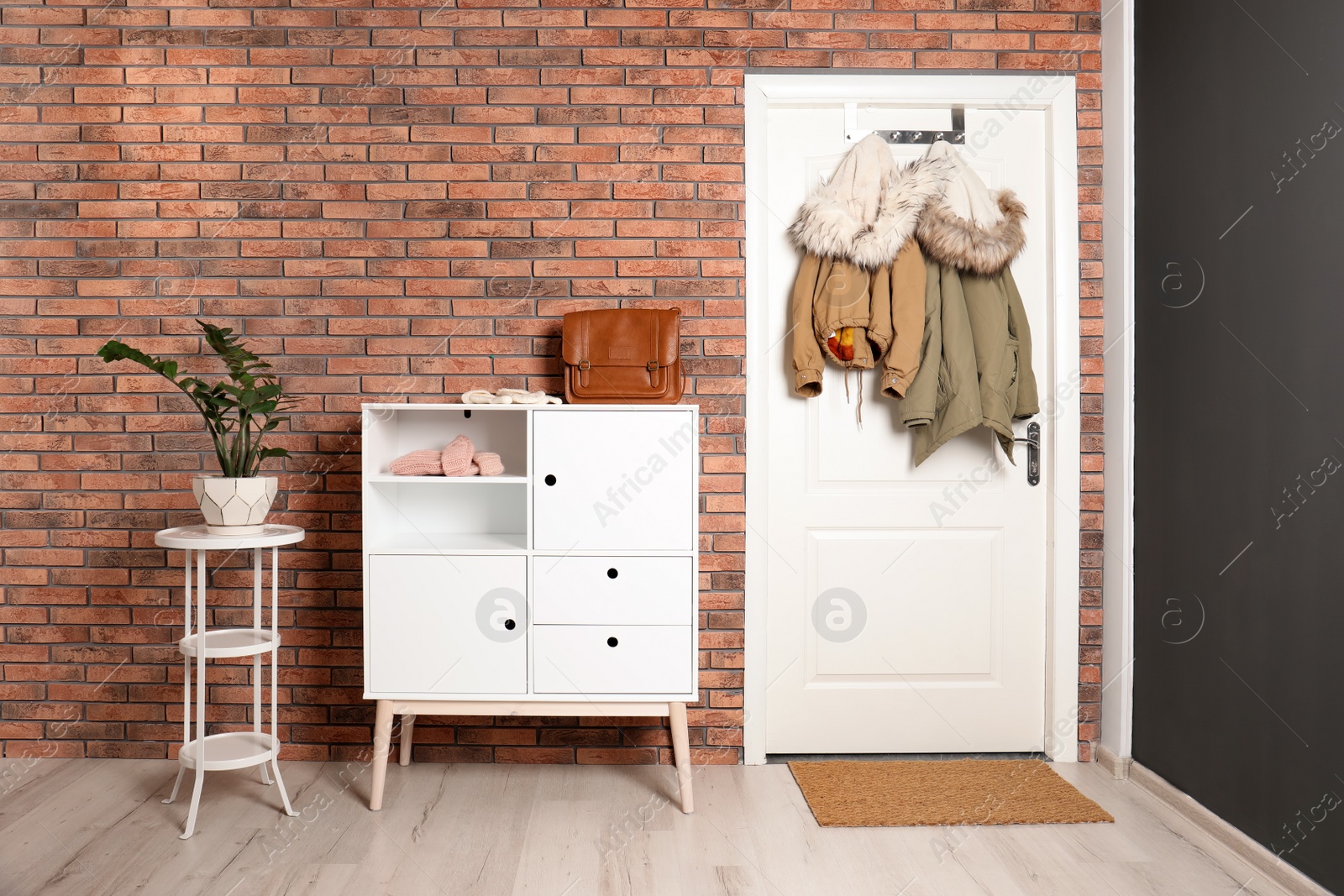 Photo of Stylish hallway interior with chest of drawers and clothes hanging on white door