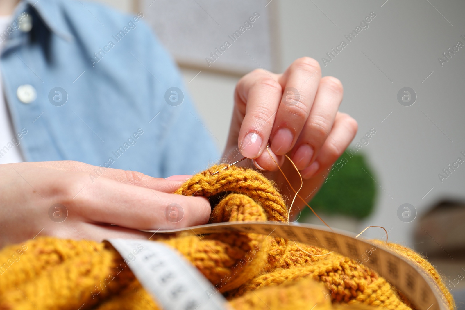 Photo of Woman sewing sweater with needle at home, closeup