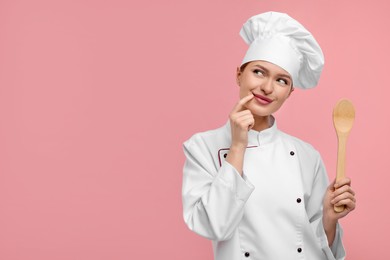 Photo of Young woman chef in uniform holding wooden spoon on pink background, space for text