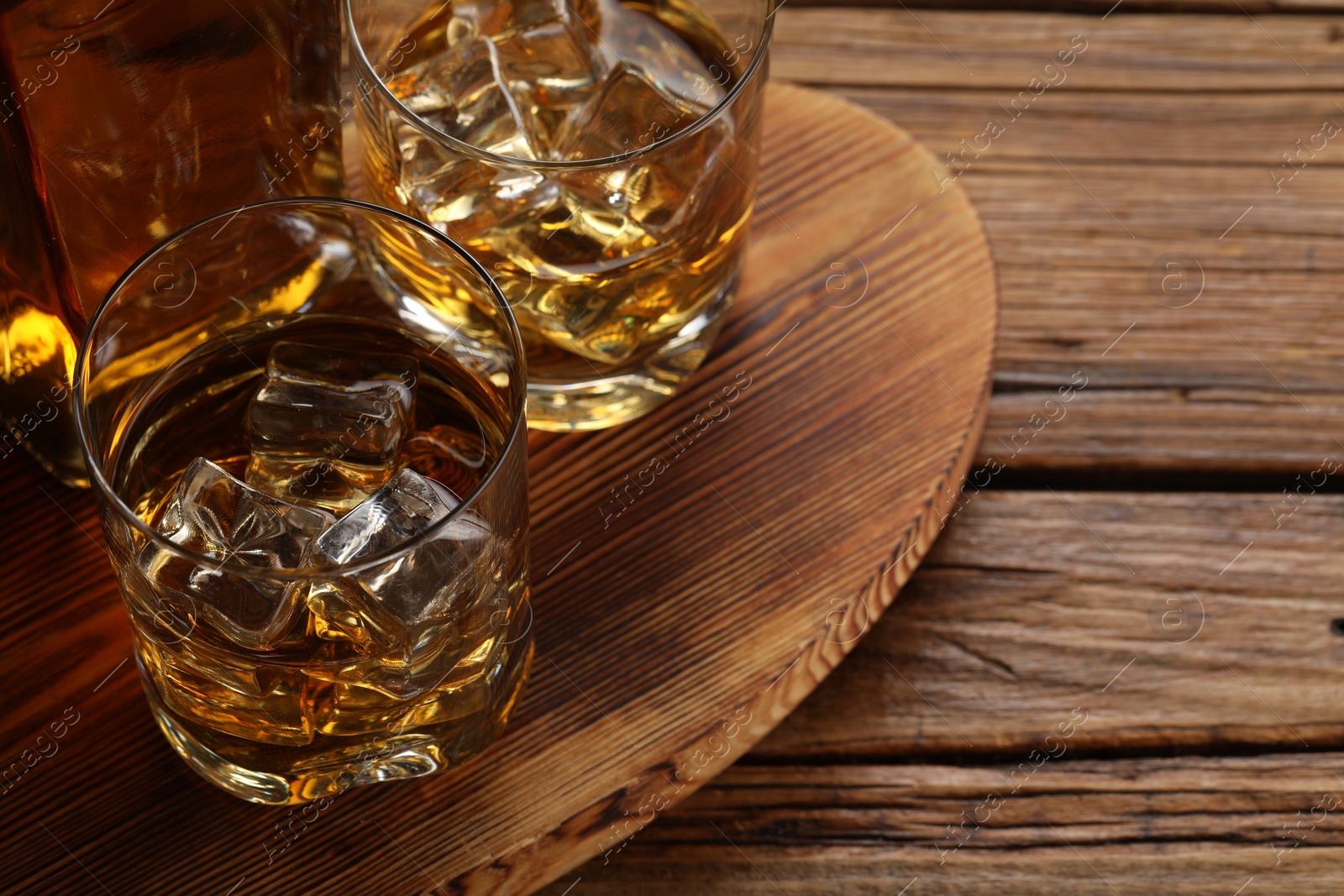 Photo of Whiskey with ice cubes in glasses and bottle on wooden table, closeup. Space for text