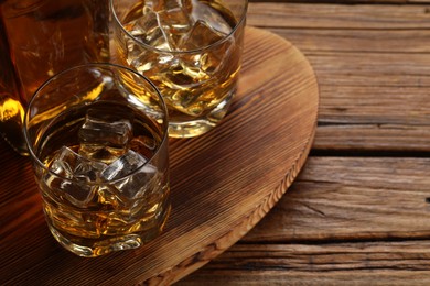 Whiskey with ice cubes in glasses and bottle on wooden table, closeup. Space for text